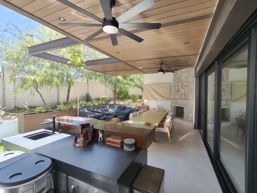 Terraza techada con plafón de madera, barra y chimenea de piedra